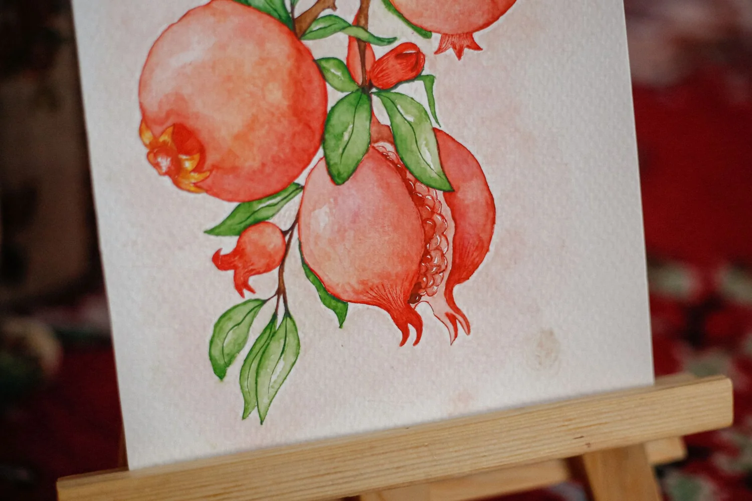 Illustration à l'aquarelle de grenades et de feuillage sur un petit chevalet en bois
